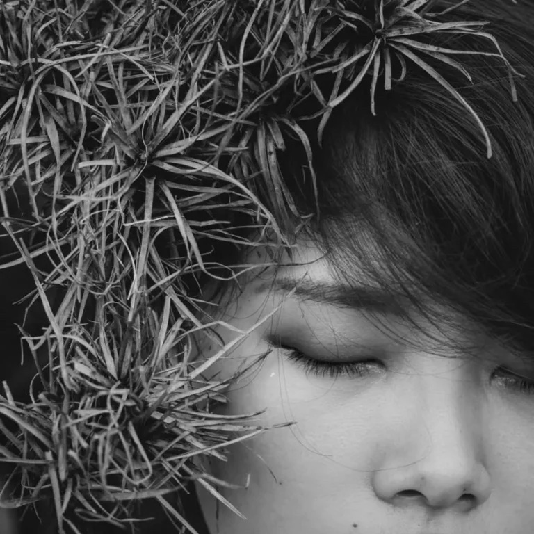 Woman with closed eyes surrounded by plants.