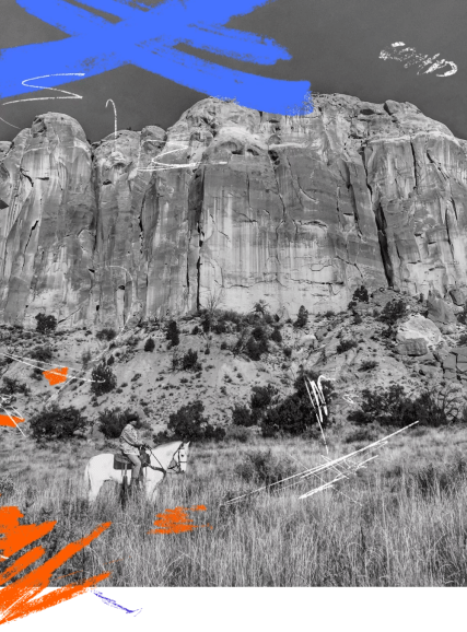 A person riding a horse near an enormous rock face